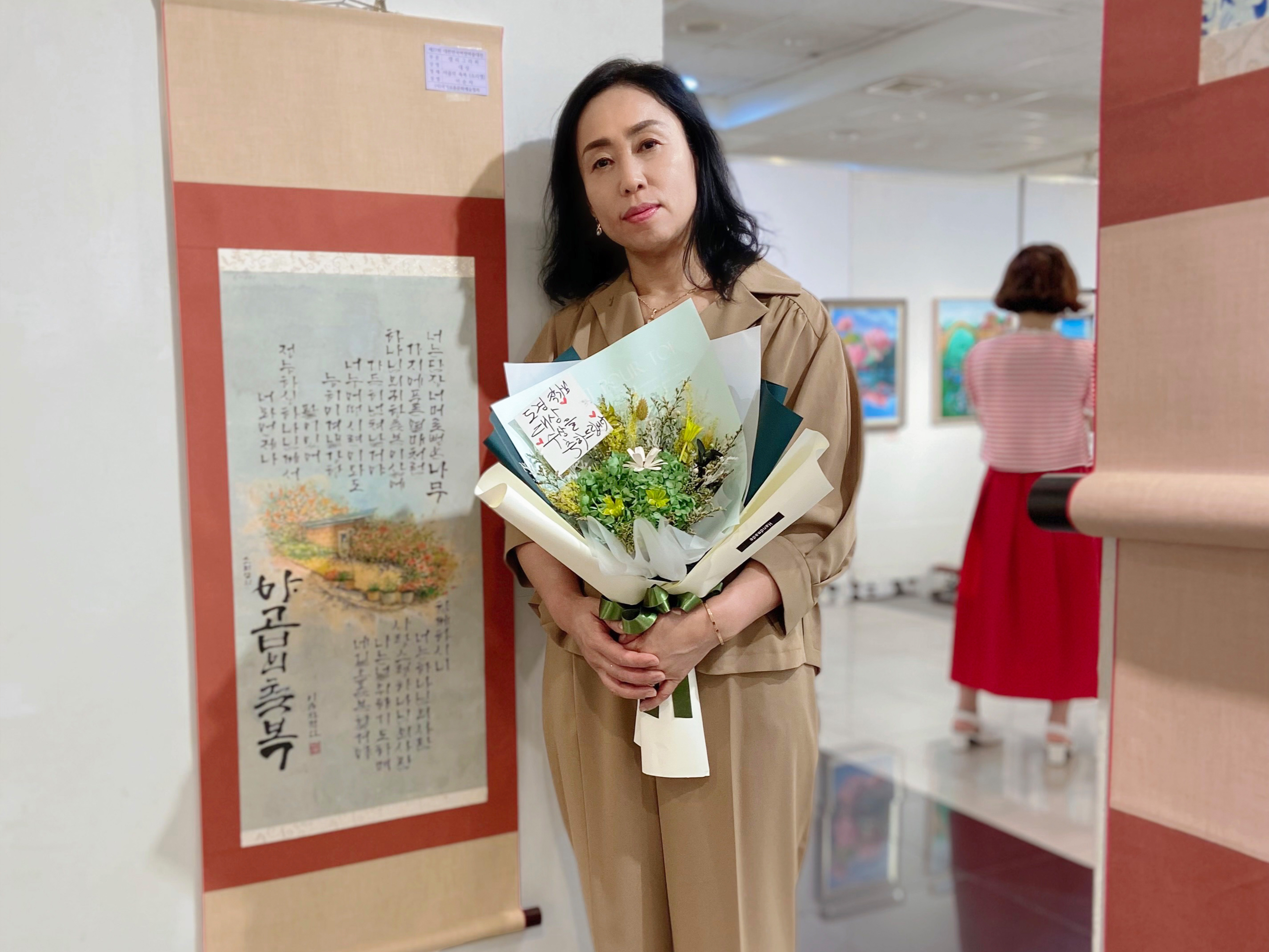 제27회 대한민국여성미술대전 전국공모 캘리그라피 부문에서 대상을 수상한 부산디지털대학교 평생교육원 기장군민대학 이순자 강사가 수상작 앞에서 기념촬영을 하고 있다.